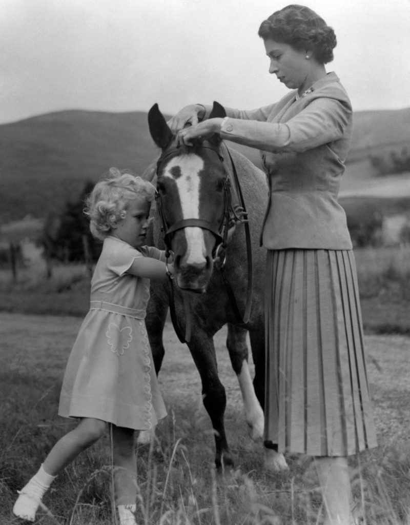 Princess Anne helps her mother Queen Elizabeth adjust the bridle of the pony 'Greensleeves' in the grounds of Balmoral on their summer holidays